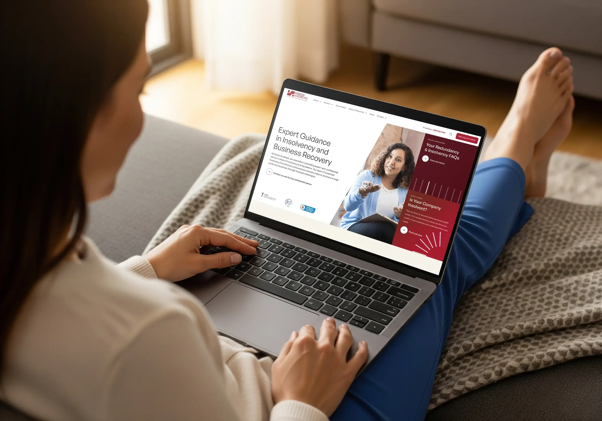 Parker Andrews mockup woman sitting on a sofa looking at a laptop with the homepage on it