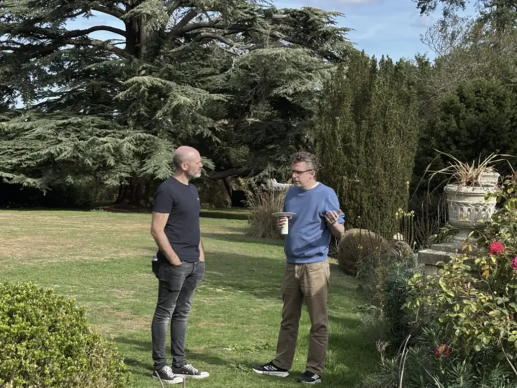 Two colleagues deep in conversation on the lawn beside a large cedar tree.