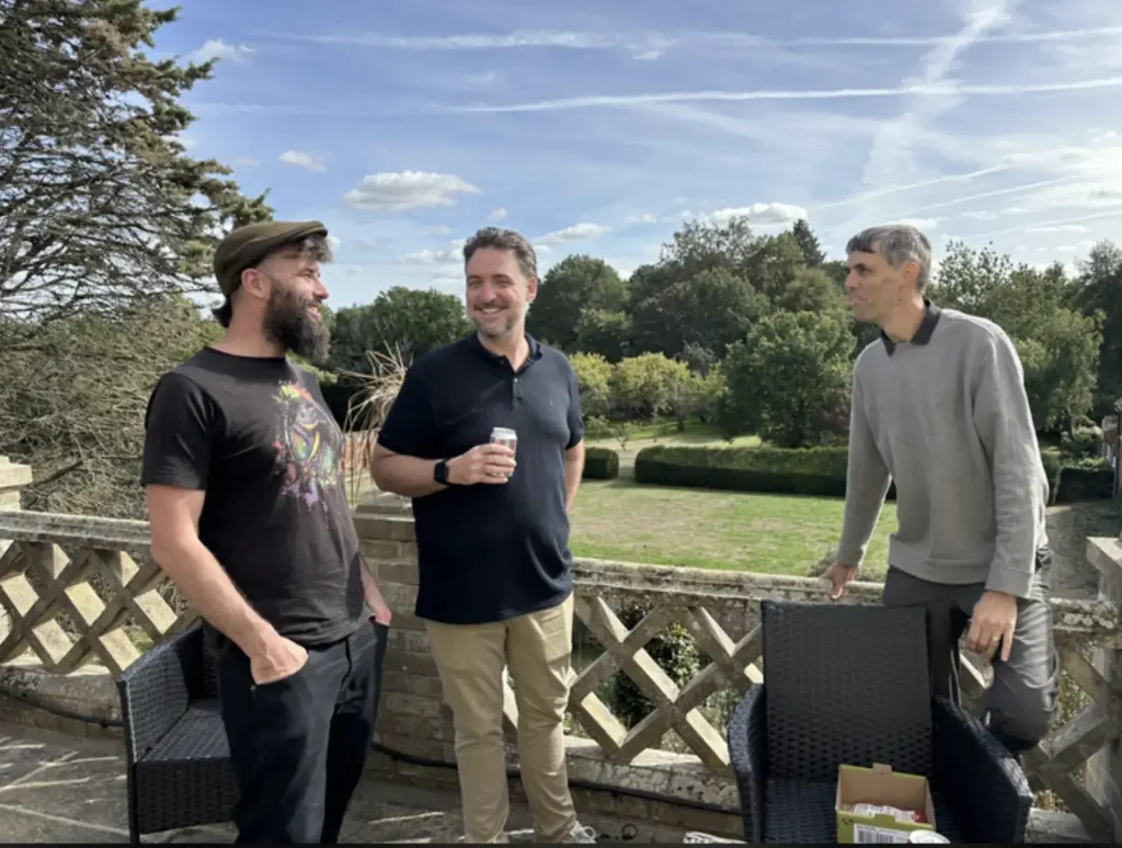 Three colleagues laughing together on the terrace, with trees and a blue sky behind them.