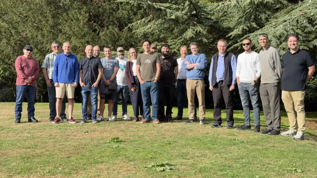 The Infotex team standing together on the lawn at Holbecks House in front of large evergreen trees on a sunny day.